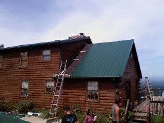 Green metal roof going on a two story log home with ladders set in Parsippany