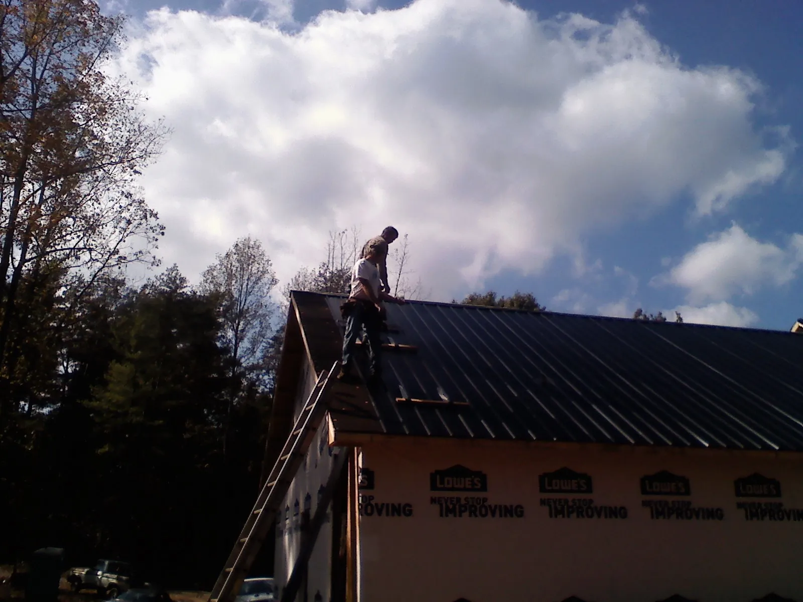 Roofer fastening dark metal panels high against a cloudy sky, from a Roof Inspection job in Parsippany