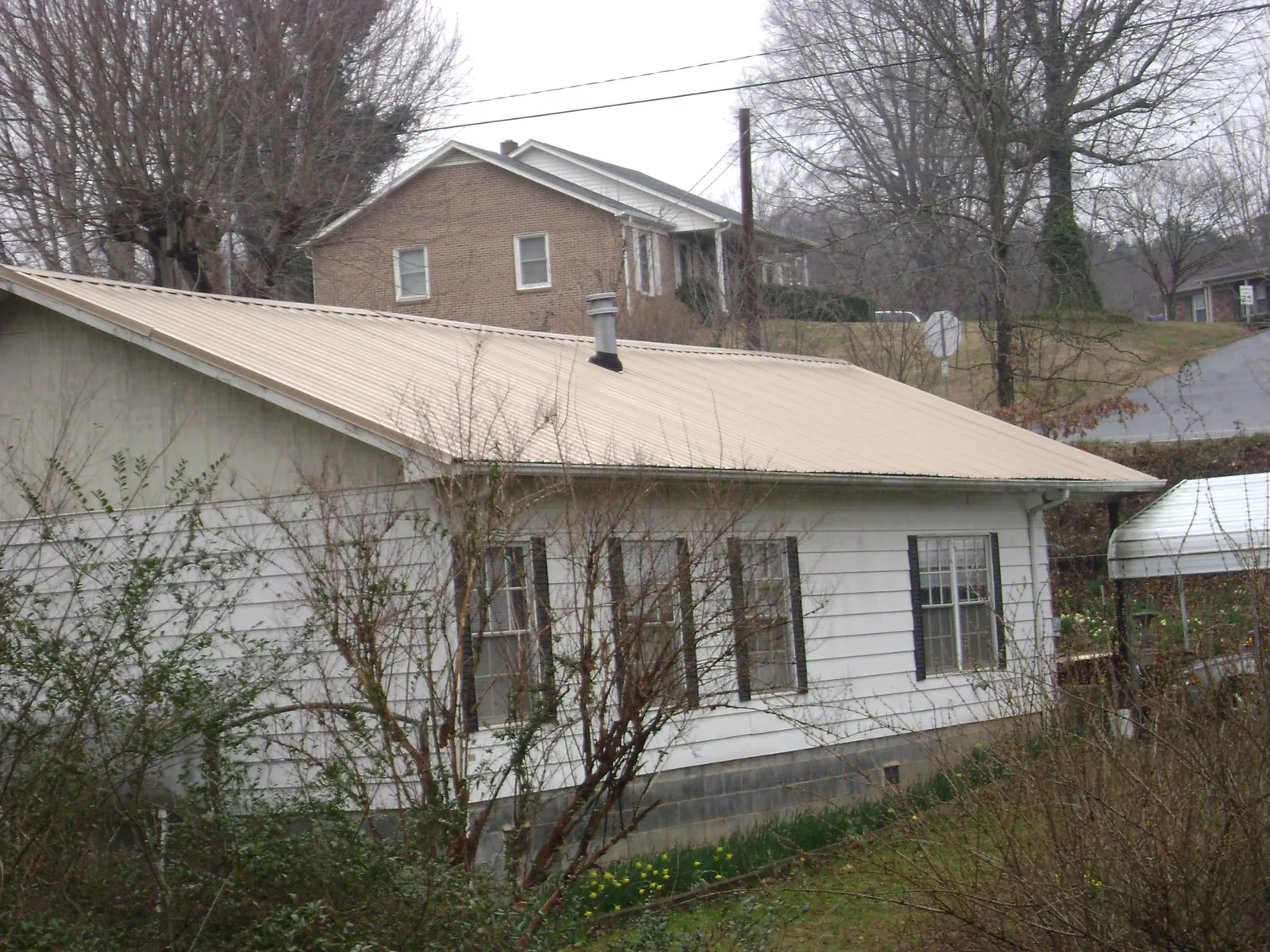 Tan metal roof on a white sided house set into a hillside — Commercial Roofing by Roofing Brothers in Parsippany